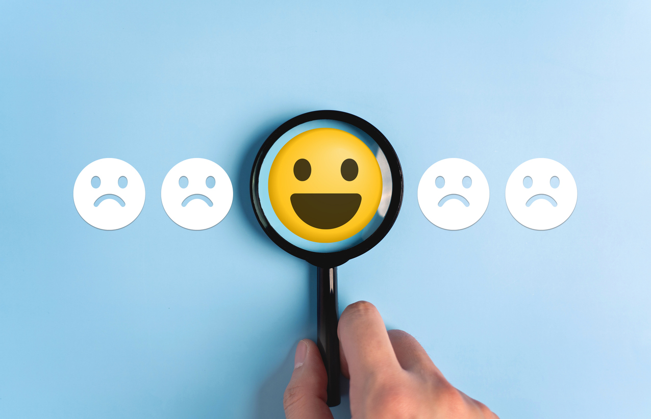 row of emoji faces, 4 grumpy and one in the middle smiling