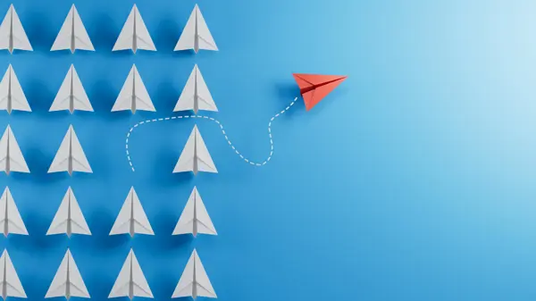 White paper planes, an orange one breaks free of the crowd